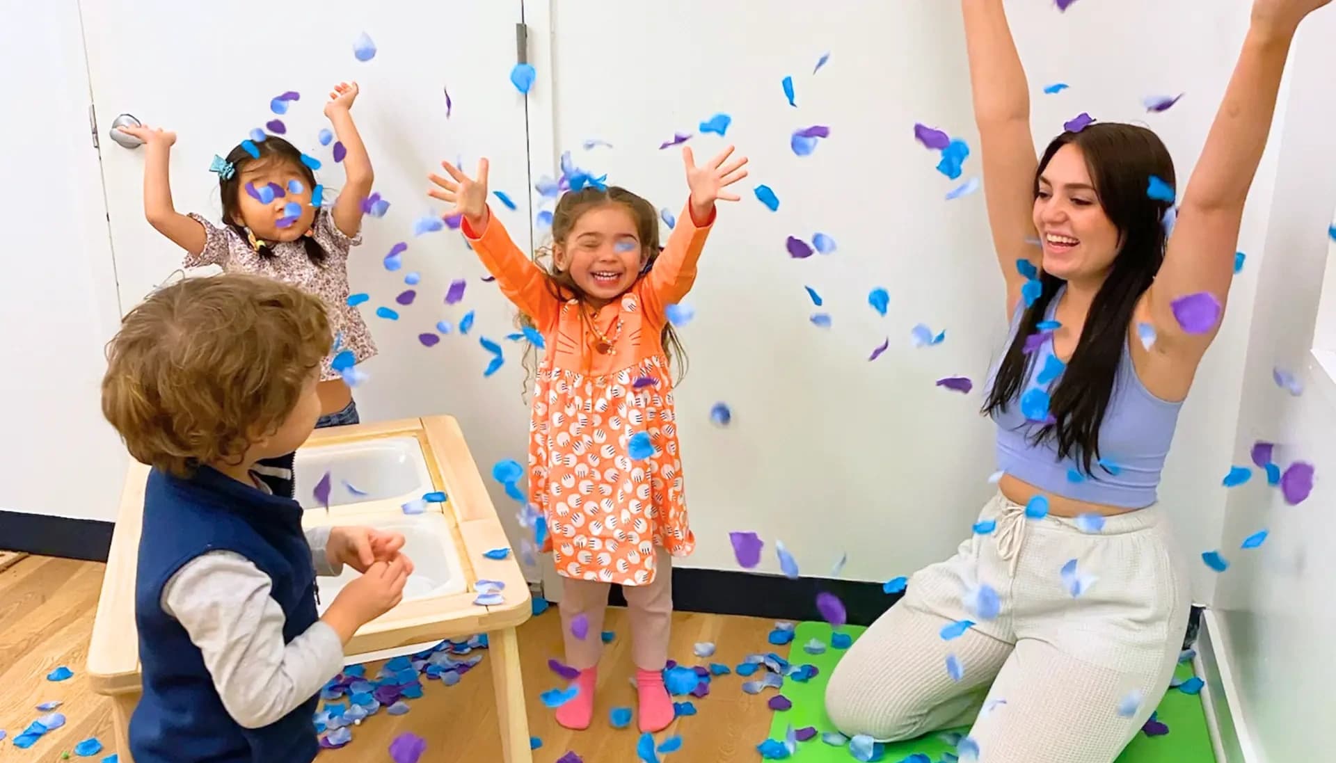 A Playgarden Prep teacher and three children celebrating under falling confetti in a classroom